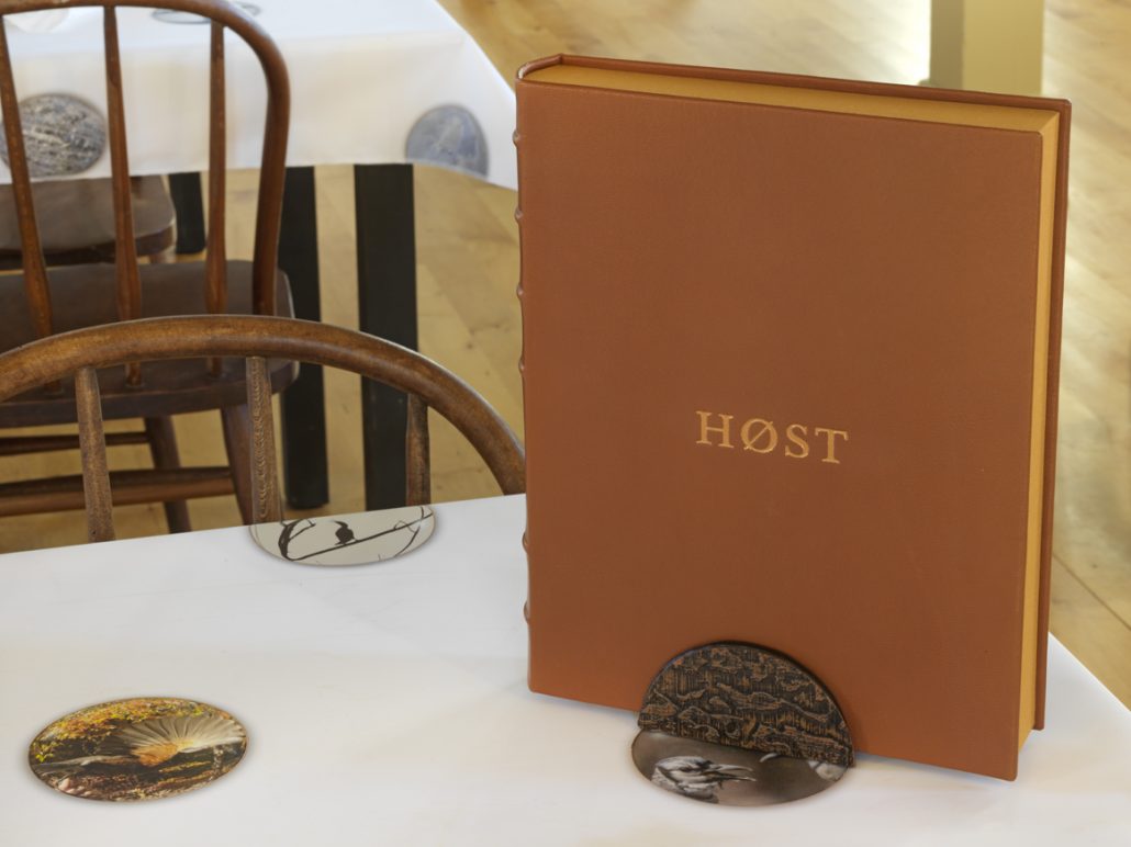 Høst Clamshell Portfolio. Leather, pigmented ink fabric, book cloth. 9.5"w x 12"h x 2"d. 2015. Book stand. Copper, leather. 4"w x 2"h x 2.5"d. 2017. Høst Tablecloth. Pigmented ink on satin. 44" x 84". 2017